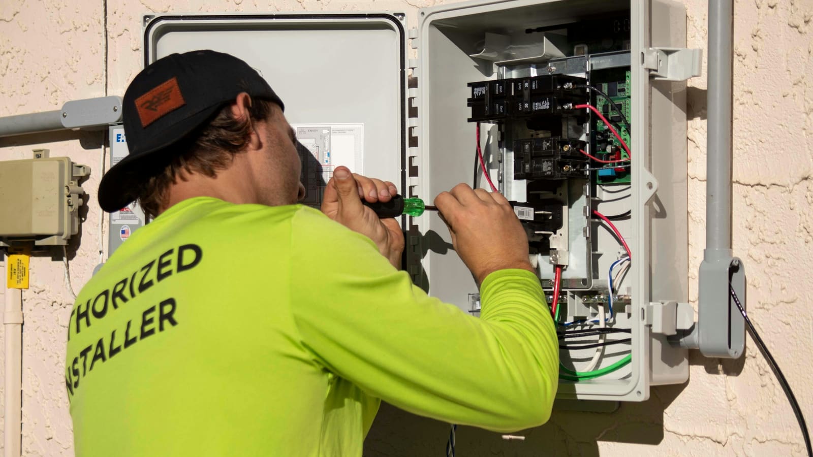 An electrician in a green shirt working on a breaker panel